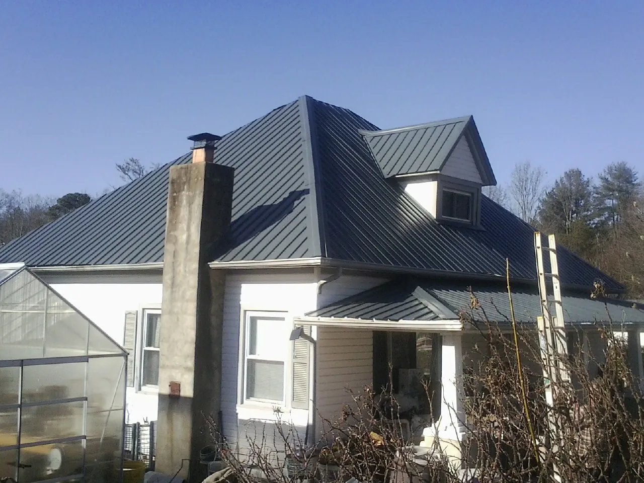 Dark blue standing seam metal roof on a white farmhouse with dormer — Slate & Tile Roof Repair by Roofing Brothers in Dwight