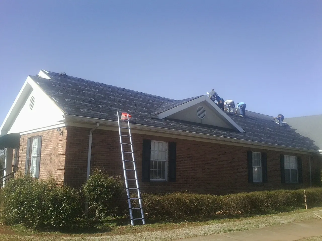 Crew tearing shingles off a brick ranch roof with a ladder set — Emergency Roof Repair work by our crew in Dwight