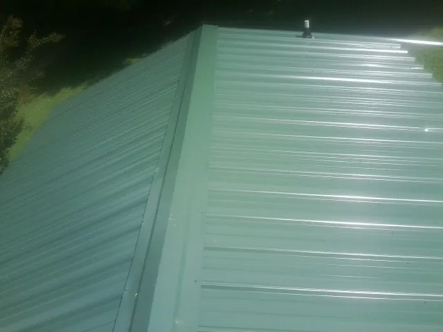 New green metal panels meeting at the ridge of a roof — Flat Roof Repair work by our crew in Dwight