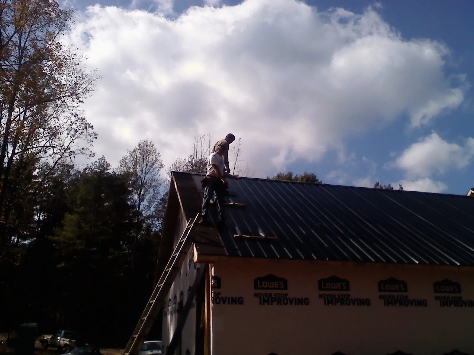 Roofer fastening dark metal panels high against a cloudy sky, from a Roof Inspection job in Dwight