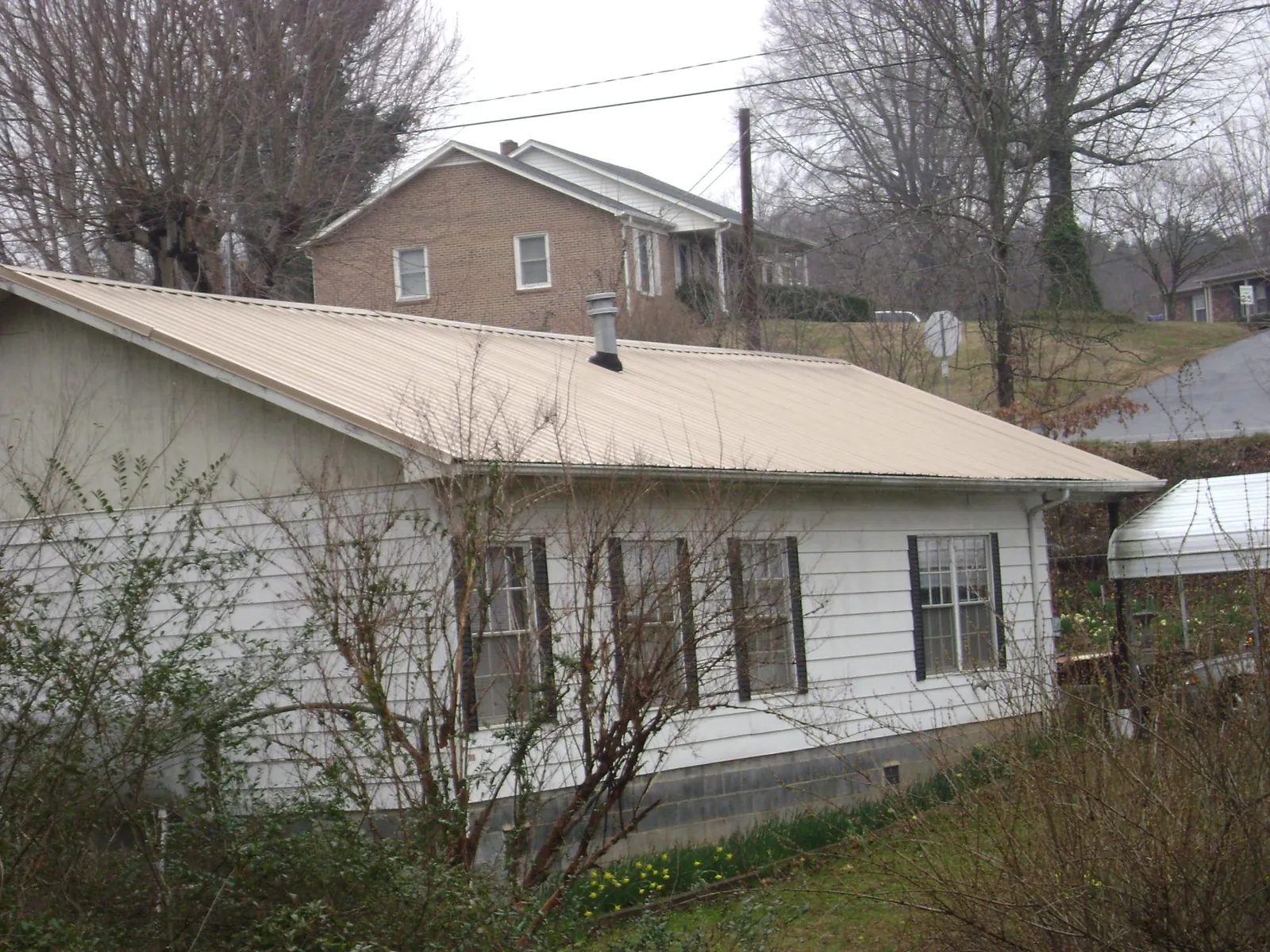 Tan metal roof on a white sided house set into a hillside — Commercial Roofing by Roofing Brothers in Dwight
